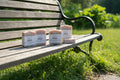 Five artisanal marbled soap bars in soft peach, cream, and pink tones, some wrapped in clear plastic with white paper labels and others stacked, displayed on a light wooden surface with green leaves in the background. 